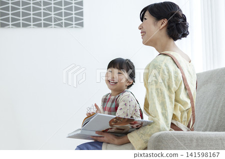 一位家長和孩子都穿著圍裙，正在沙發上看書。 141598167