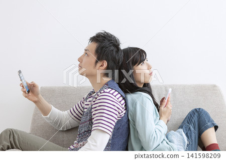 A couple looking at their cell phones on the sofa A couple looking at their cell phones on the sofa 141598209
