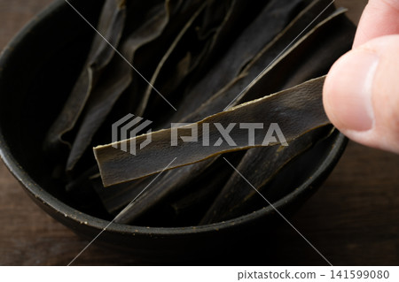 Close-up of a piece of kelp being held between fingers. Close-up of a piece of kelp being held between fingers. 141599080