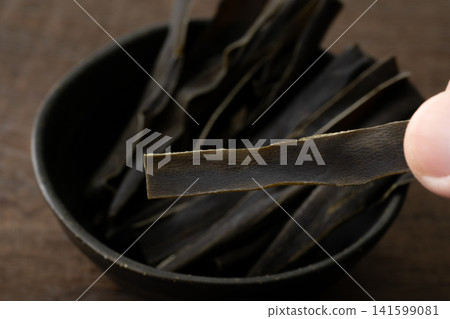 Close-up of a piece of kelp being held between fingers. 141599081