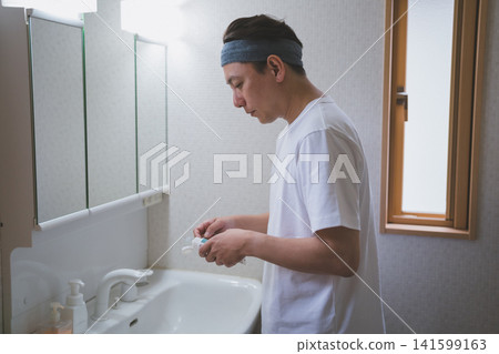 一位四十多歲、戴著髮帶的男子在浴室裡往牙刷上擠牙膏。 一位四十多歲、戴著髮帶的男子在浴室裡往牙刷上擠牙膏。 141599163