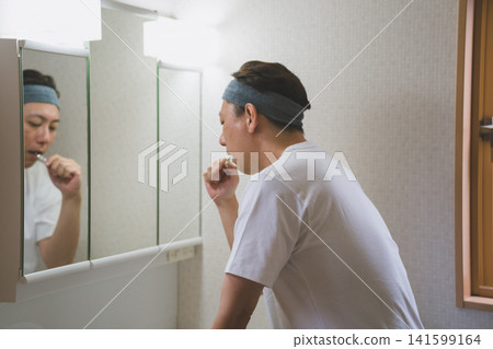 A man in his 40s brushing his teeth in the bathroom while wearing a headband. A man in his 40s brushing his teeth in the bathroom while wearing a headband. 141599164