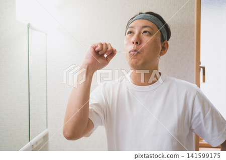 一名四十多歲的男子戴著髮帶在浴室刷牙。 一名四十多歲的男子戴著髮帶在浴室刷牙。 141599175