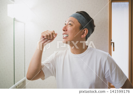一名四十多歲的男子戴著髮帶在浴室刷牙。 一名四十多歲的男子戴著髮帶在浴室刷牙。 141599176