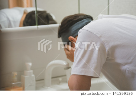 一名四十多歲的男子戴著髮帶,在水槽邊洗臉。 一名四十多歲的男子戴著髮帶,在水槽邊洗臉。 141599186