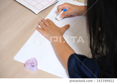 孩子的手正在擦掉筆記本上的字跡。 孩子的手正在擦掉筆記本上的字跡。 141599922