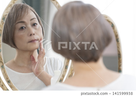 一位老年婦女在鏡子前進行護膚步驟。 一位老年婦女在鏡子前進行護膚步驟。 141599938
