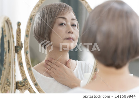 一位老年婦女在鏡子前進行護膚步驟。 一位老年婦女在鏡子前進行護膚步驟。 141599944