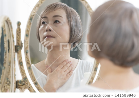 一位老年婦女在鏡子前進行護膚步驟。 一位老年婦女在鏡子前進行護膚步驟。 141599946