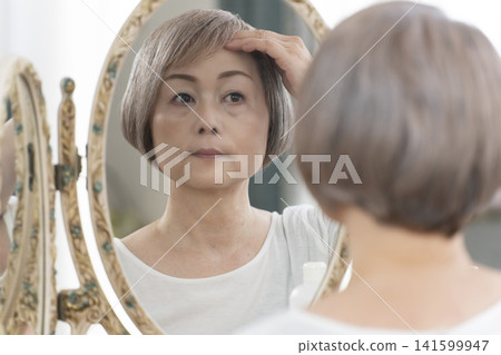 一位老年婦女在鏡子前進行護膚步驟。 一位老年婦女在鏡子前進行護膚步驟。 141599947