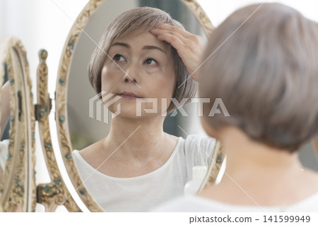 一位老年婦女在鏡子前進行護膚步驟。 一位老年婦女在鏡子前進行護膚步驟。 141599949