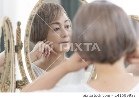 一位老年婦女在鏡子前進行護膚步驟。 一位老年婦女在鏡子前進行護膚步驟。 141599952