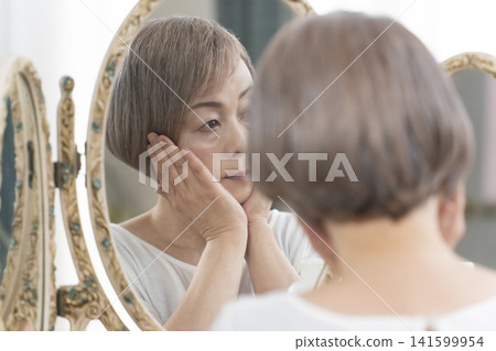 Senior woman doing her skincare routine in front of the mirror Senior woman doing her skincare routine in front of the mirror 141599954