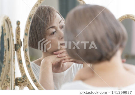 一位老年婦女在鏡子前進行護膚步驟。 一位老年婦女在鏡子前進行護膚步驟。 141599957