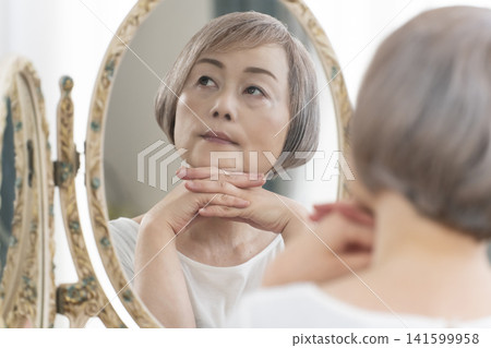 一位老年婦女在鏡子前進行護膚步驟。 一位老年婦女在鏡子前進行護膚步驟。 141599958