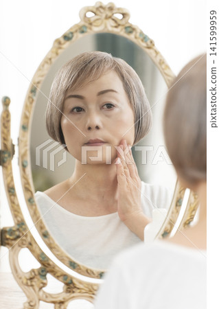 一位老年婦女在鏡子前進行護膚步驟。 一位老年婦女在鏡子前進行護膚步驟。 141599959