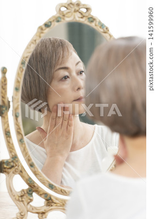 一位老年婦女在鏡子前進行護膚步驟。 一位老年婦女在鏡子前進行護膚步驟。 141599960