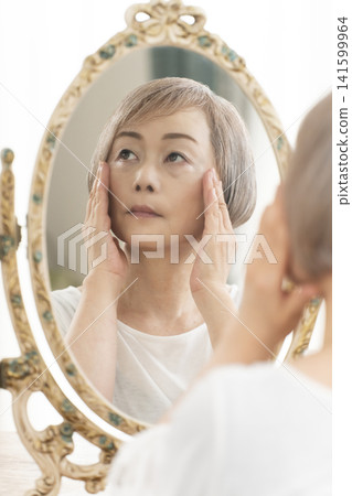 一位老年婦女在鏡子前進行護膚步驟。 一位老年婦女在鏡子前進行護膚步驟。 141599964