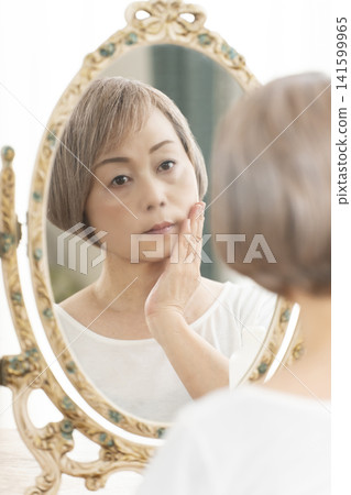 一位老年婦女在鏡子前進行護膚步驟。 一位老年婦女在鏡子前進行護膚步驟。 141599965