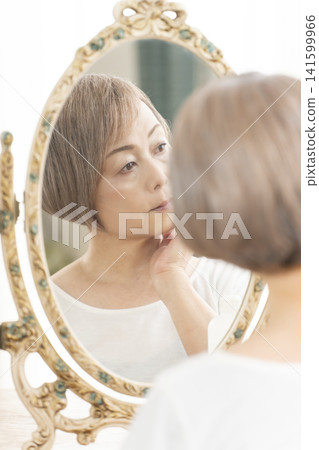 一位老年婦女在鏡子前進行護膚步驟。 一位老年婦女在鏡子前進行護膚步驟。 141599966