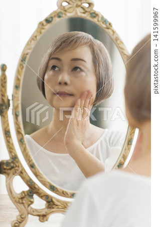 一位老年婦女在鏡子前進行護膚步驟。 一位老年婦女在鏡子前進行護膚步驟。 141599967