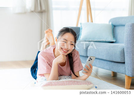 在房間裡操作智慧型手機的年輕女子 在房間裡操作智慧型手機的年輕女子 141600053
