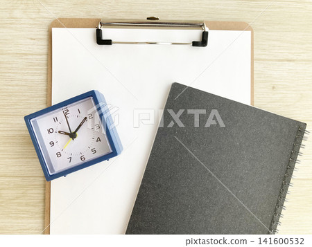 A blue clock and a black notebook are placed on the clipboard - for time management and scheduling. 141600532