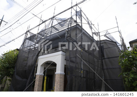 一棟獨立式住宅正在進行外牆粉刷和翻新,周圍搭起了黑色防護網和鷹架。 一棟獨立式住宅正在進行外牆粉刷和翻新,周圍搭起了黑色防護網和鷹架。 141601245