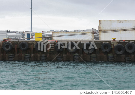 An industrial harbor dock lined with large tire fenders and stacked shipping containers 141601467