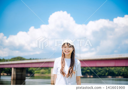夏日的天空下，一位戴著白色帽子的女子在河邊微笑。 141601900