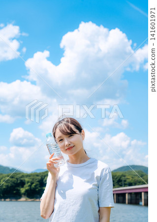 夏天，一名女子在河邊拿著一個塑膠瓶。 141601971