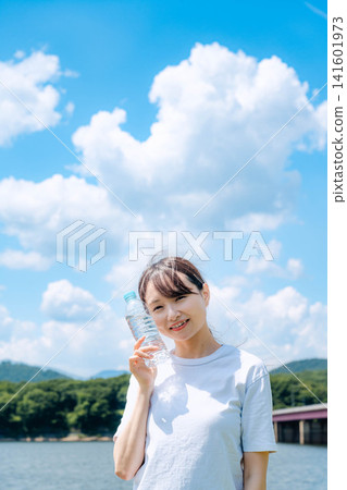 A woman in a white T-shirt drinking water with cumulonimbus clouds in the background. A woman in a white T-shirt drinking water with cumulonimbus clouds in the background. 141601973