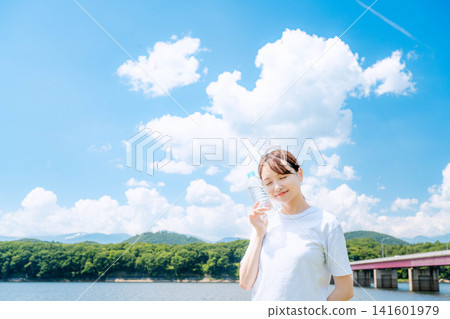 A woman smiling and holding a bottle under a blue sky 141601979