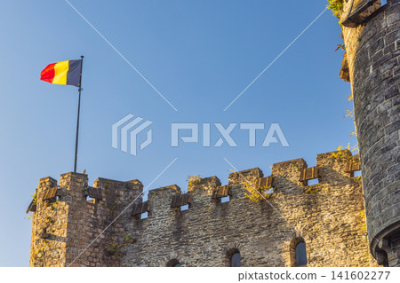 Gravensteen, a medieval castle in the city of Ghent in Belgium, Europe. Historic Stone Fortress Walls Beneath a Clear Blue Sky with a Brightly Colored Flag Waving Gravensteen, a medieval castle in the city of Ghent in Belgium, Europe. Historic Stone Fortress Walls Beneath a Clear Blue Sky with a Brightly Colored Flag Waving 141602277