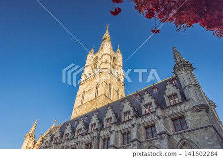 Ghent town in Belgium, Europe. Low Angle View of Historic Belfry Tower and Grand Building with Clear Blue Sky and Hint of Autumn Foliage Ghent town in Belgium, Europe. Low Angle View of Historic Belfry Tower and Grand Building with Clear Blue Sky and Hint of Autumn Foliage 141602284
