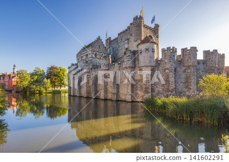 Gravensteen, a medieval castle in the city of Ghent in Belgium, Europe. Historic Stone Fortress with Turrets Reflected in Calm River Water Under a Bright Blue Sky on a Sunny Day Gravensteen, a medieval castle in the city of Ghent in Belgium, Europe. Historic Stone Fortress with Turrets Reflected in Calm River Water Under a Bright Blue Sky on a Sunny Day 141602291