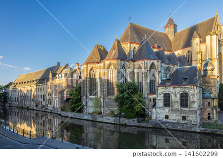Ghent town in Belgium, Europe. Saint Michael's Church, Historic European Architecture Reflected in Canal Water Under a Clear Blue Sky on a Sunny Day, Showcasing Old-World Charm Ghent town in Belgium, Europe. Saint Michael's Church, Historic European Architecture Reflected in Canal Water Under a Clear Blue Sky on a Sunny Day, Showcasing Old-World Charm 141602299