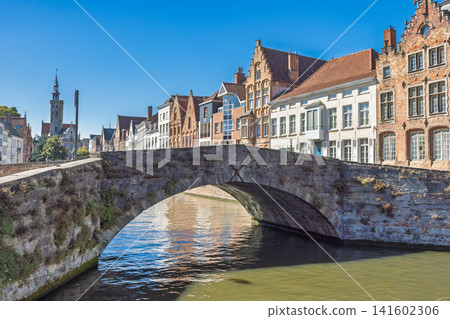 Bruges town in Belgium, Europe. Historic Stone Bridge Arching Over a Serene Canal Adorned with Picturesque Traditional European Architecture Under Blue Sky Bruges town in Belgium, Europe. Historic Stone Bridge Arching Over a Serene Canal Adorned with Picturesque Traditional European Architecture Under Blue Sky 141602306