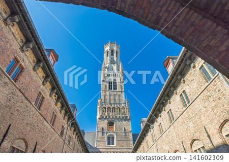 The Belfry of Bruges, a medieval bell tower in Bruges town in Belgium, Europe. Historic European Bell Tower Against a Clear Blue Sky, Framed by Traditional Brick Buildings, Showcasing Old-World Charm The Belfry of Bruges, a medieval bell tower in Bruges town in Belgium, Europe. Historic European Bell Tower Against a Clear Blue Sky, Framed by Traditional Brick Buildings, Showcasing Old-World Charm 141602309