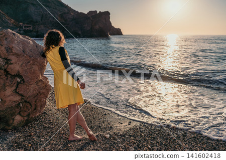 Woman beach sunset overlooking the ocean while leaning on a rock at dusk 141602418