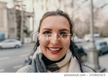 Woman portrait city smiling lady wearing wool scarf and coat on a bright urban street during autumn morning light 141602423