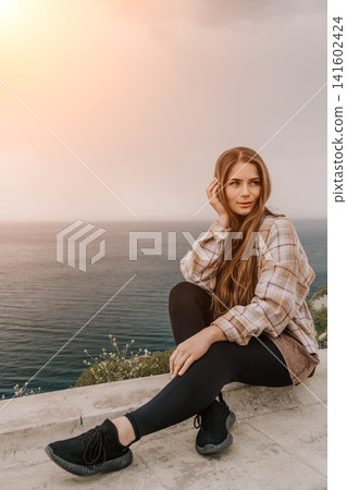 Woman sunset ocean sitting on a stone wall overlooking the sea with copy space for inspirational text Woman sunset ocean sitting on a stone wall overlooking the sea with copy space for inspirational text 141602424