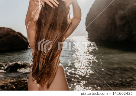 Woman bikini sunset Young brunette woman in white swimwear standing on a rocky coastline during a golden hour summer vacation Woman bikini sunset Young brunette woman in white swimwear standing on a rocky coastline during a golden hour summer vacation 141602425
