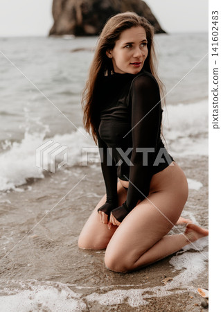 Woman beach ocean kneeling on wet sand as waves splash around her during a serene summer day at the coast Woman beach ocean kneeling on wet sand as waves splash around her during a serene summer day at the coast 141602483