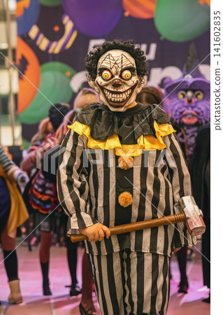 Participant wearing a striped clown costume and mask poses with toy hammer during Halloween costume contest. Halloween parade, disguise, celebration, festival entertainment, public event Participant wearing a striped clown costume and mask poses with toy hammer during Halloween costume contest. Halloween parade, disguise, celebration, festival entertainment, public event 141602835