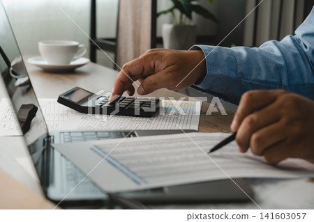 man use calculator and write on financial documents beside a laptop, showing figure checking and report review workflow for accounting, budgeting, and business finance content. man use calculator and write on financial documents beside a laptop, showing figure checking and report review workflow for accounting, budgeting, and business finance content. 141603057