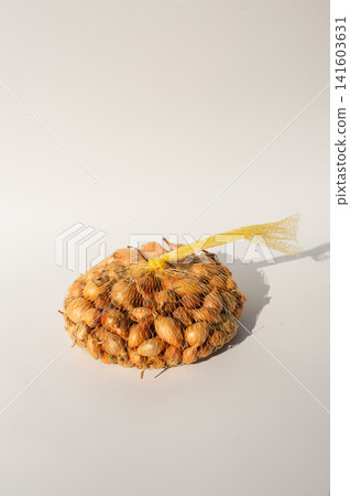 Mesh bag of yellow onions on white surface with shadows Mesh bag of yellow onions on white surface with shadows 141603631