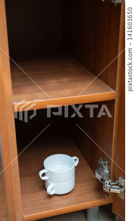 Empty wooden cabinet with linked white two-handled cups on lower shelf Empty wooden cabinet with linked white two-handled cups on lower shelf 141603650
