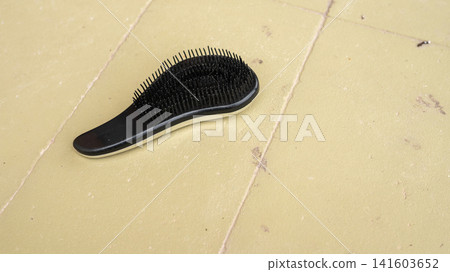 Black hairbrush on yellow tile floor with loose bristles Black hairbrush on yellow tile floor with loose bristles 141603652