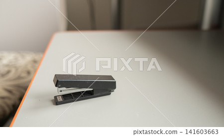 Black stapler on a gray table with wooden edge in a minimalist office setting Black stapler on a gray table with wooden edge in a minimalist office setting 141603663